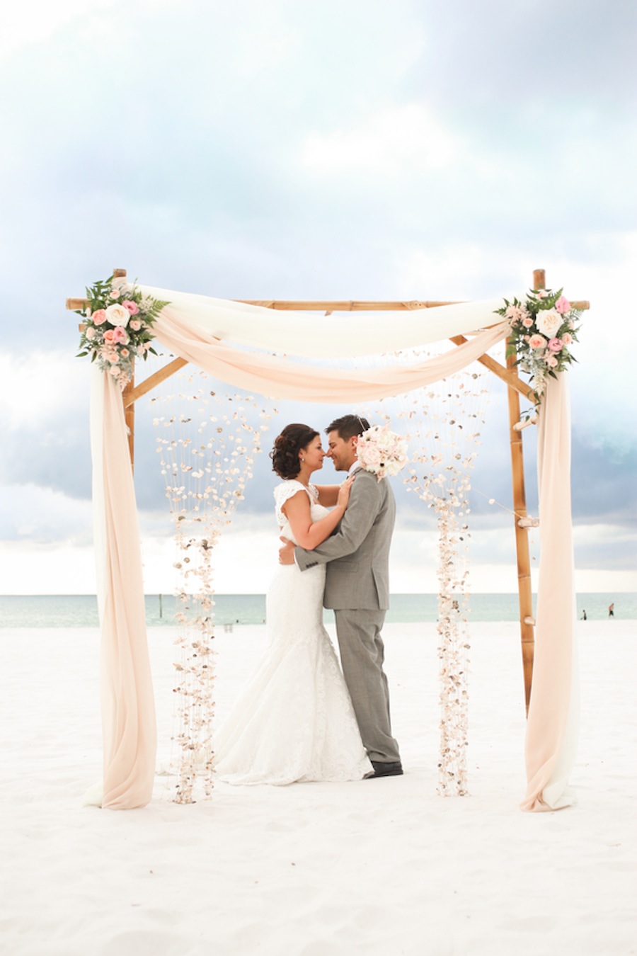 Bride and Groom Clearwater Beach Wedding Ceremony with Bamboo Alter and Pastel Pink Flowers and Hanging Seashells