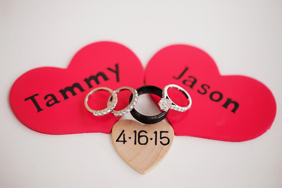 Bride and Groom Engagement Ring and Wedding Bands on Wooden Heart with Wedding Dates