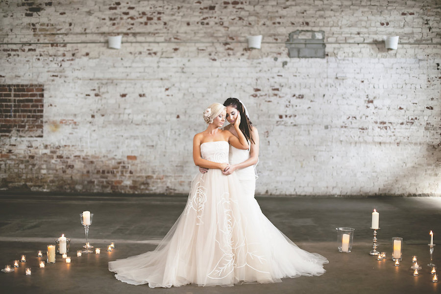 Same Sex Gay Brides Embracing in Blush and Ivory Strapless Wedding Gowns Surrounded By Candles Wedding Portrait | Tampa Wedding Venue Rialto Theater | Wedding Photographer FotoBohemia