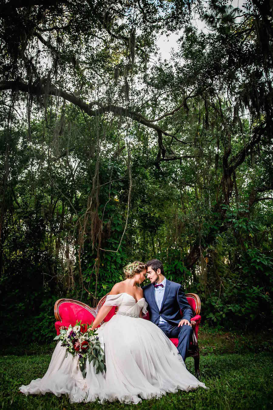 Bride in Amsale Wedding Dress from Blush Bridal Sarasota with Deep Red Burgundy Wedding Bouquet with Greenery on Red Vintage Couch Chaise | Southern Inspired Outdoor Wedding Reception Decor Styled Shoot