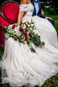 Bride in Amsale Wedding Dress from Blush Bridal Sarasota with Deep Red Burgundy Wedding Bouquet with Greenery on Red Vintage Couch Chaise | Southern Inspired Outdoor Wedding Reception Decor Styled Shoot