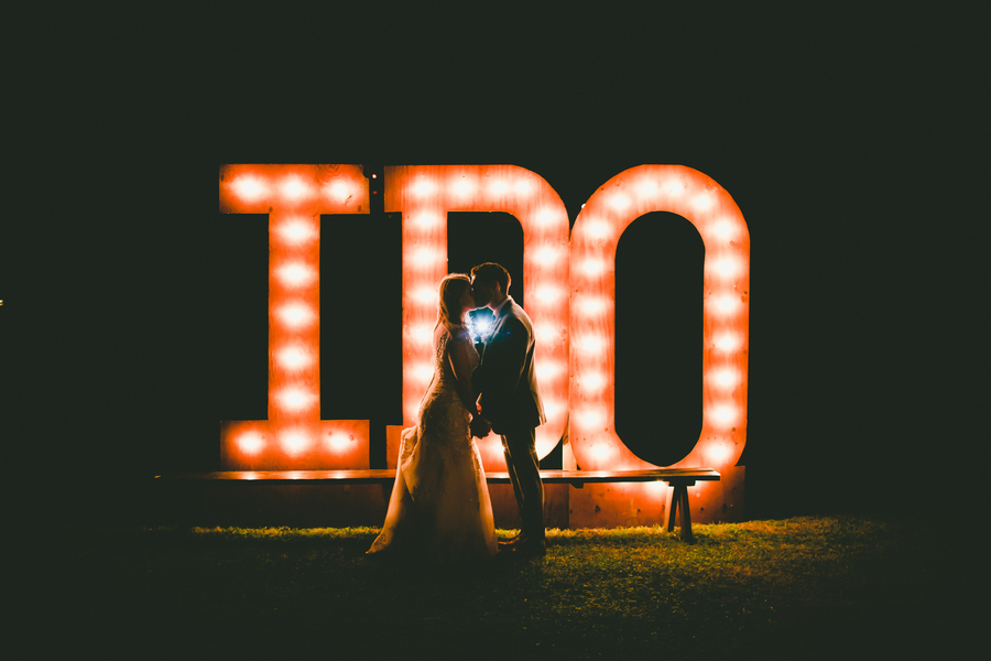 Bride and Groom Kissing in Front of I Do Wedding Sign With Lights