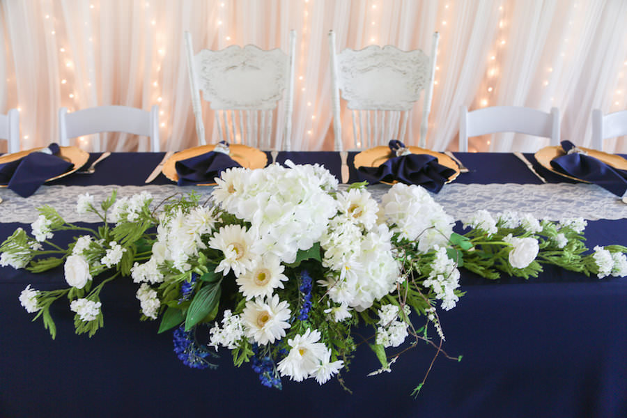 Rustic Wedding Reception Sweetheart Table Decor with White and Blue Floral Centerpiece, Navy Linens, Lace Runner and Gold Chargers | Tampa Bay Wedding Venue Cross Creek Ranch