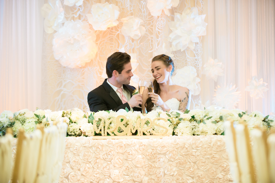 Bride and Groom Cheers Champagne Glasses at Gold and Ivory Wedding Reception Sweetheart Table | Brooksville Wedding Venue Southern Hills Plantation Club
