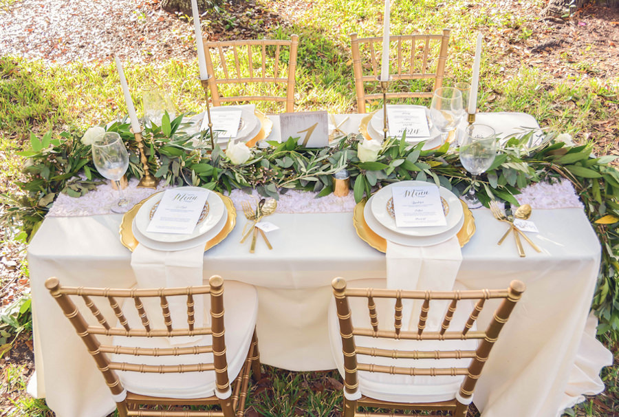 Wedding Reception Tablescape with Lush Greenery Table Runner with Gold Candle Sticks with Gold Chargers with Gold Silverware with Ivory Linens with Gold Chiavra| Andrea Layne Floral Design | Kate Ryan Custom Linens