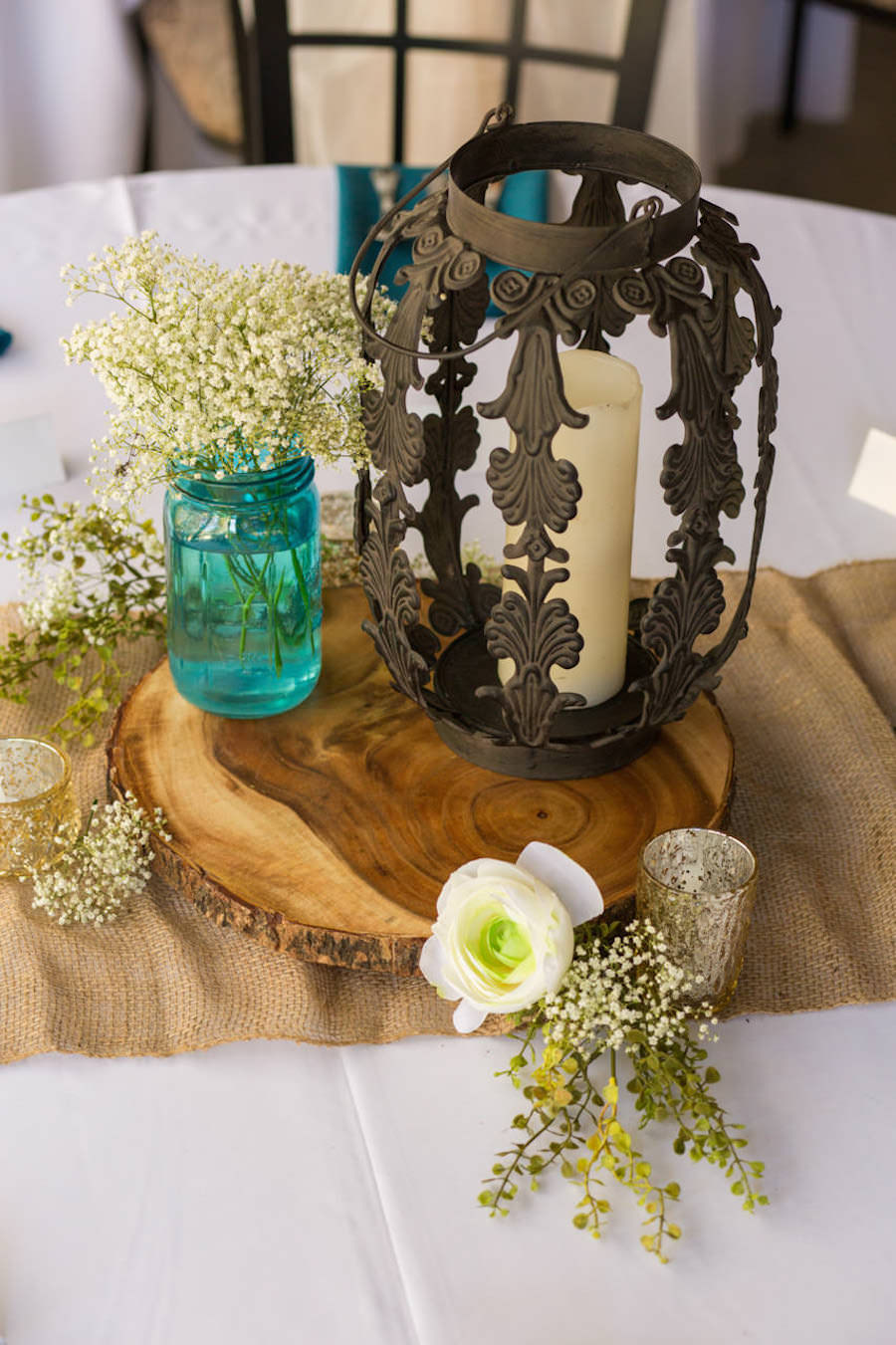 Rustic Wedding Reception Table Decor with Wooden Slab, Baby's Breath in Blue Mason Jars, and Vintage Candle Lanterns