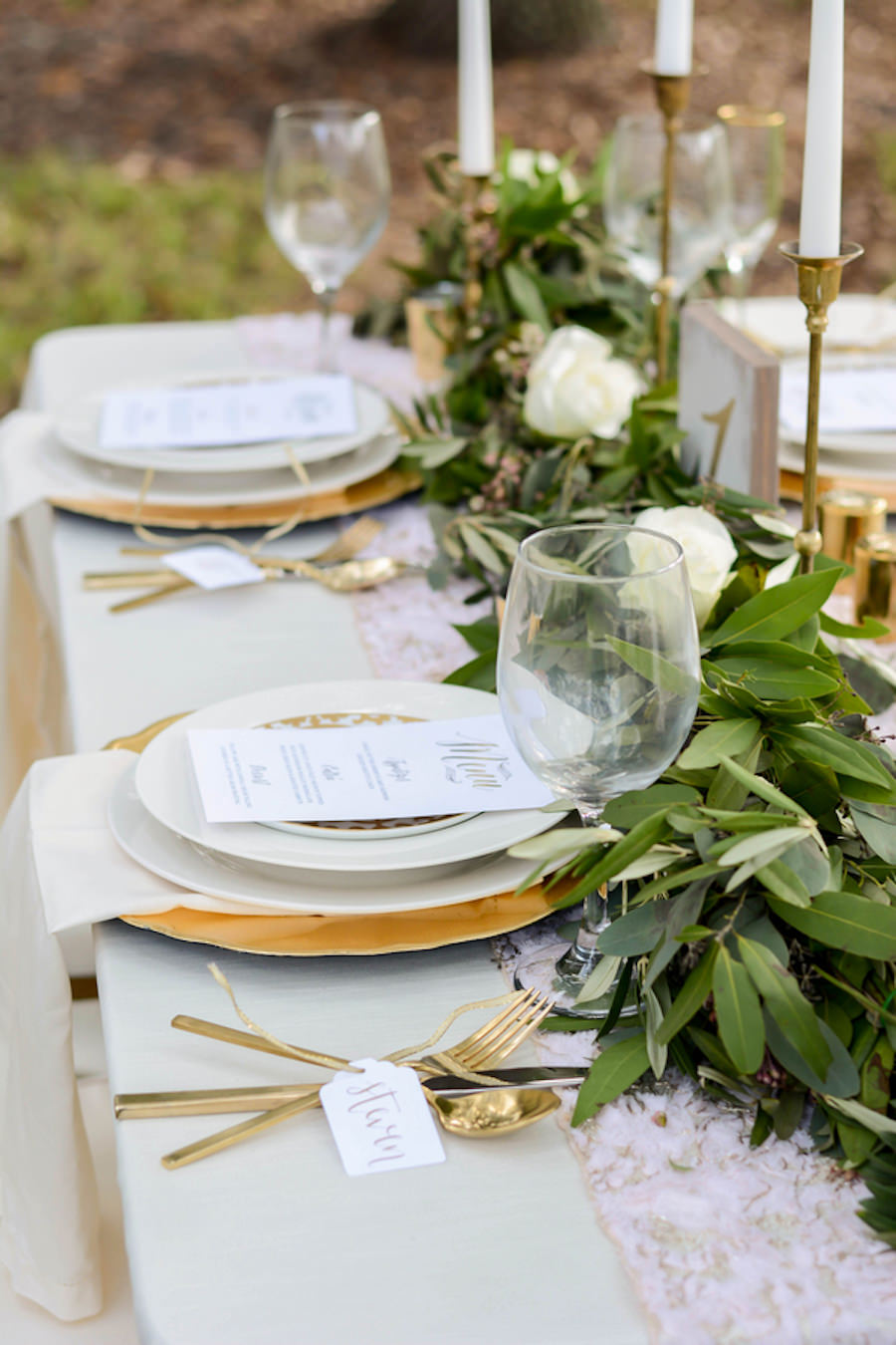 Wedding Reception Tablescape with Lush Greenery Table Runner with Gold Candle Sticks with Gold Chargers with Gold Silverware with Ivory Linens | Andrea Layne Floral Design | Kate Ryan Custom Linens