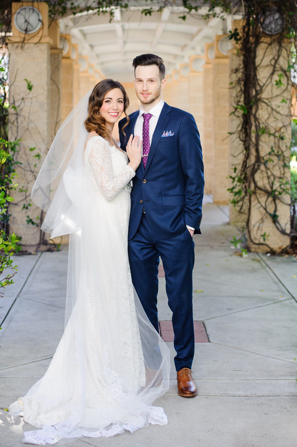 Bride and Groom Wedding Portrait | Mikaella Bridal Lace Wedding Dress with Sleeves and Groom in Navy Blue Suit with Tan Shoes