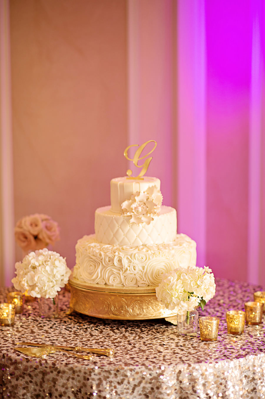 Three Tied Round White Wedding Cake with Rose and Quilt Pattern and Gold Initial Cake Topper on Sequined Specialty Linen