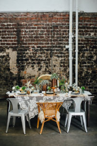 Tampa Nature Inspired Wedding Reception Table Decor with Wooden Farm Table, Mismatched Chairs, Brass, Greenery Centerpieces, Crystal Goblets, Wooden Place Settings, and Doily TableCloth