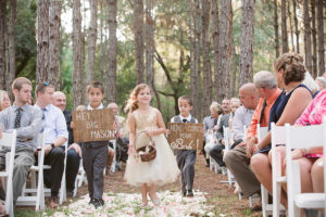 Flower Girl and Ring Bearers Walking Down the Ceremony Aisle with Rustic, Wooden Signs