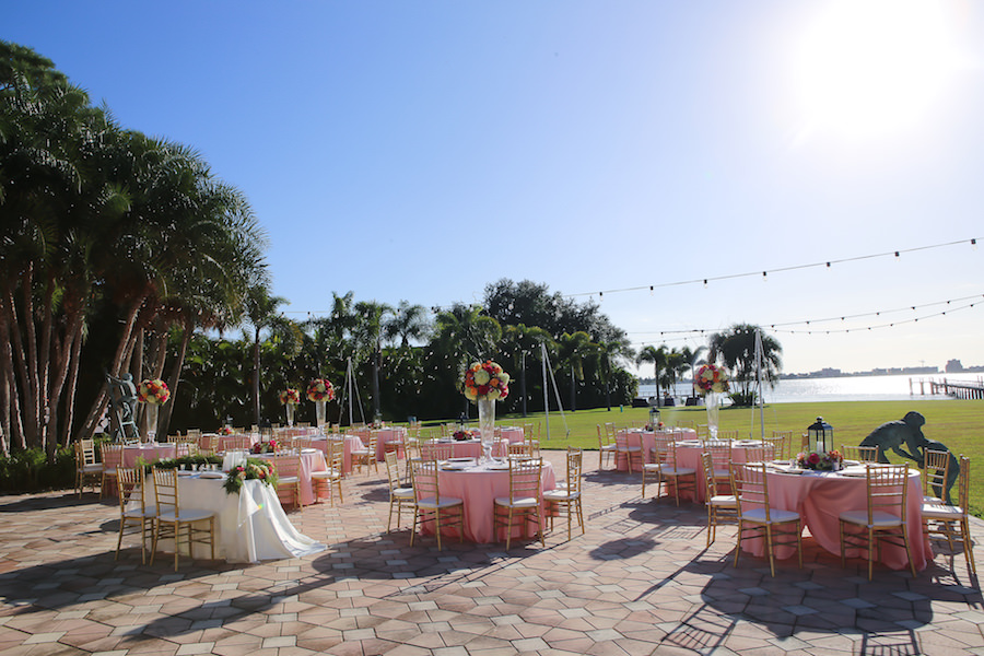 Waterfront Outdoor St Petersburg Wedding Reception Décor with Gold Chiavari Chairs, Pink Linens and Orange, Bright Pink and Fuchsia Floral Centerpieces with Twinkle Market Lights | Exquisite Events Wedding Planning