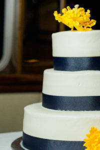 Round Three-Tier White Wedding Cake with Navy Ribbon and Yellow Sugar Flowers