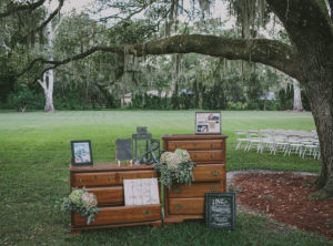 Outdoor, Rustic Sarasota Wedding Ceremony Guest Table with Card Lantern, Pictures, and Floral Arrangement on Vintage Wooden Chest of Drawers Furinture