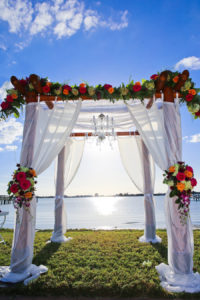St Petersburg Waterfront Wedding Ceremony under Floral Arch with Fuchsia and Orange Roses, Greenery and Tulle Overlay | St. Petersburg Wedding Planner Exquisite Events