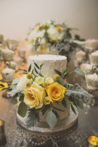 Two Tier Round White Wedding Cake with Yellow Roses and Greenery on Silver Cake Stand with Love Cake Topper