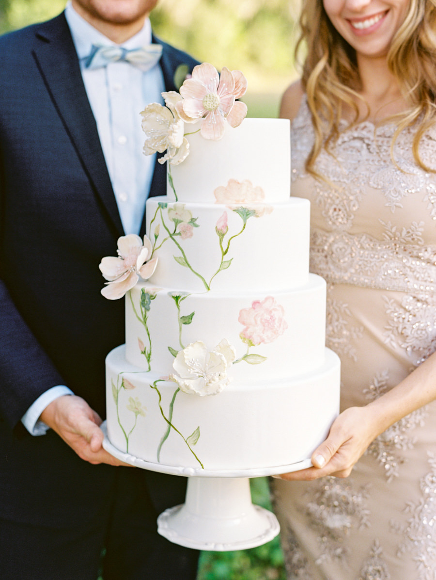 Bride and Groom Wedding Portrait with Four Tiered Round White Wedding Cake with Watercolor Painted Blush Flowers and Green Stems with Gumpaste Flowers on Ivory Wedding Cake Stand