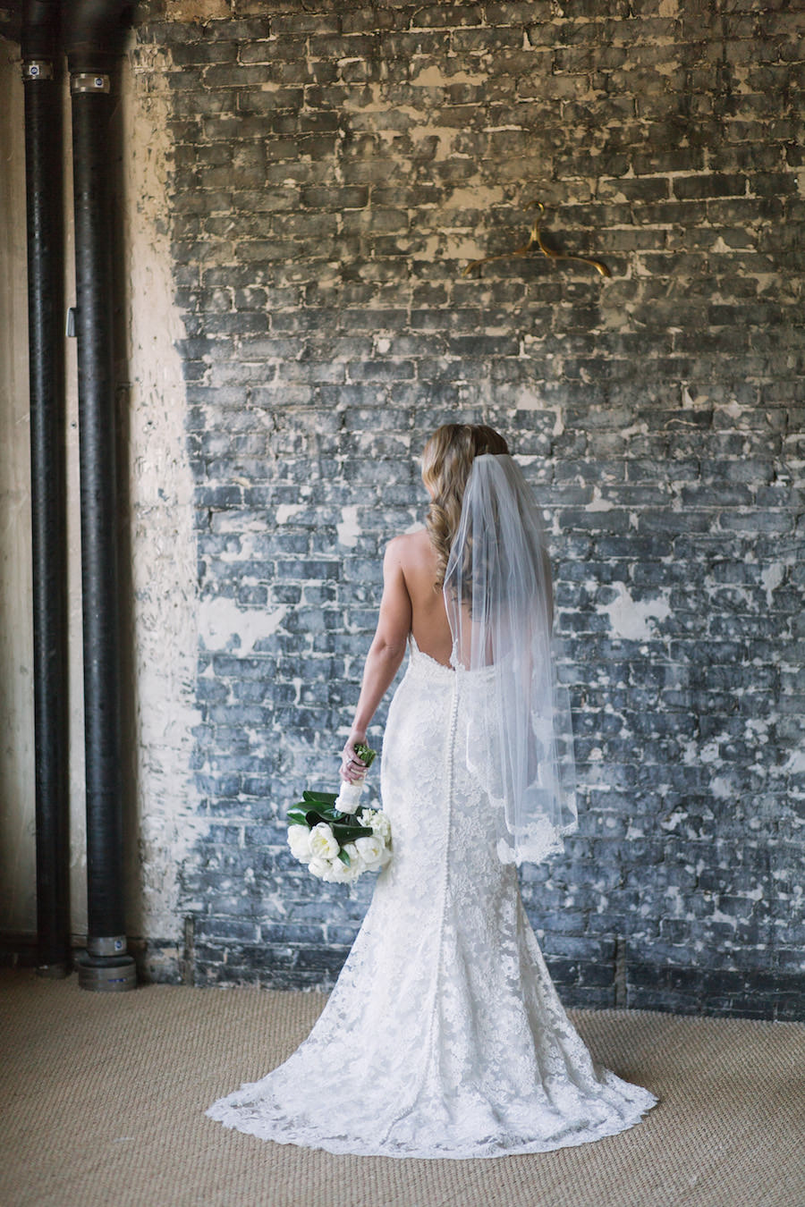 Bridal Wedding Portrait in Ivory, Lace Strapless Dress, Lace Veil, and White Floral Wedding Bouquet of Flowers with Industrial Brick Wall Backdrop