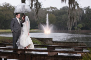 Outdoor, Bride and Groom Wedding Portrait on Dock with Fountain and Umbrella During Rain in Ivory, Lace Wedding Gown | Wedding Photographer Carrie Wildes Photography | Tampa Wedding Venue Tampa Palms Golf and Country Club