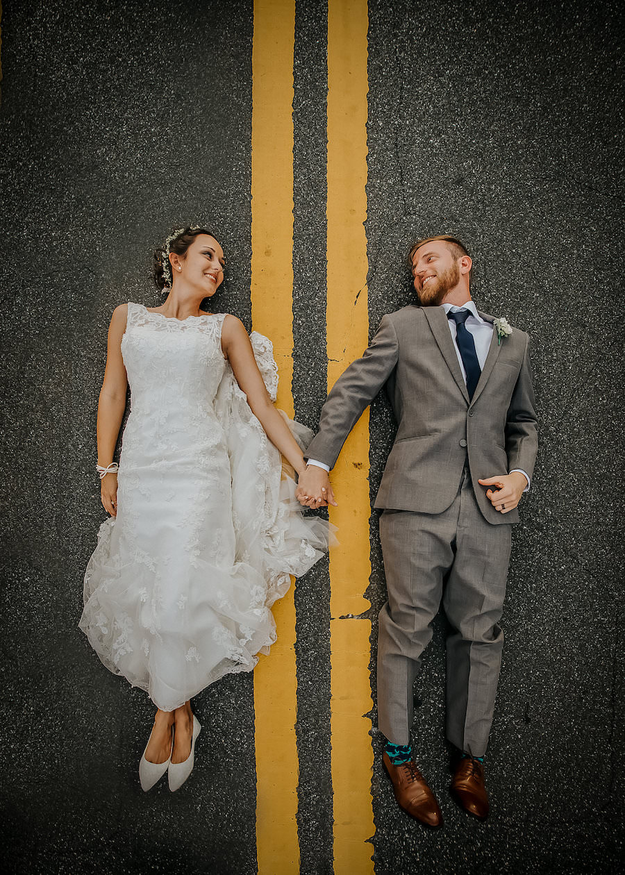 Outdoor, Bride and Groom Wedding Portrait Laying in Road in Ivory, Lace Wedding Dress and Grey Groom's Suit | Lakeland Wedding Photographer Rad Red Creative