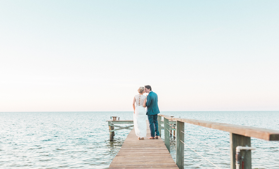 Outdoor, Waterfront Tampa Bay Bride and Groom Wedding Portrait on Boardwalk in Ivory, Allure Wedding Dress and Blue Groom's Suit