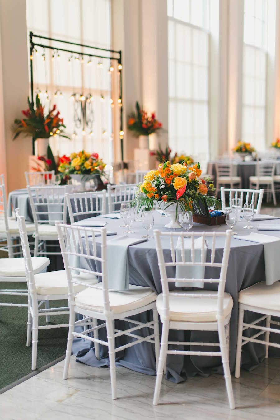 Tropical Wedding Reception Décor with Gray Table Linens and Bright Yellow and Orange Floral Wedding Centerpieces with White Chiavari Chairs | Tampa Wedding Planner Blush by Brandee Gaar | Photography by Roohi Photography | Downtown Tampa Wedding Venue The Vault