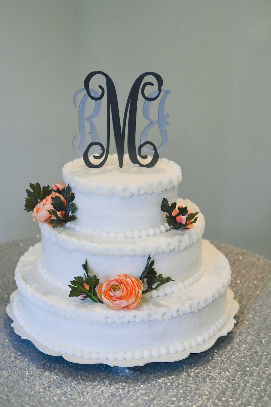 Three Tier Round White Wedding Cake with Coral Roses and Pearl Trim with Monogram Cake Topper on Sequined Specialty Linen