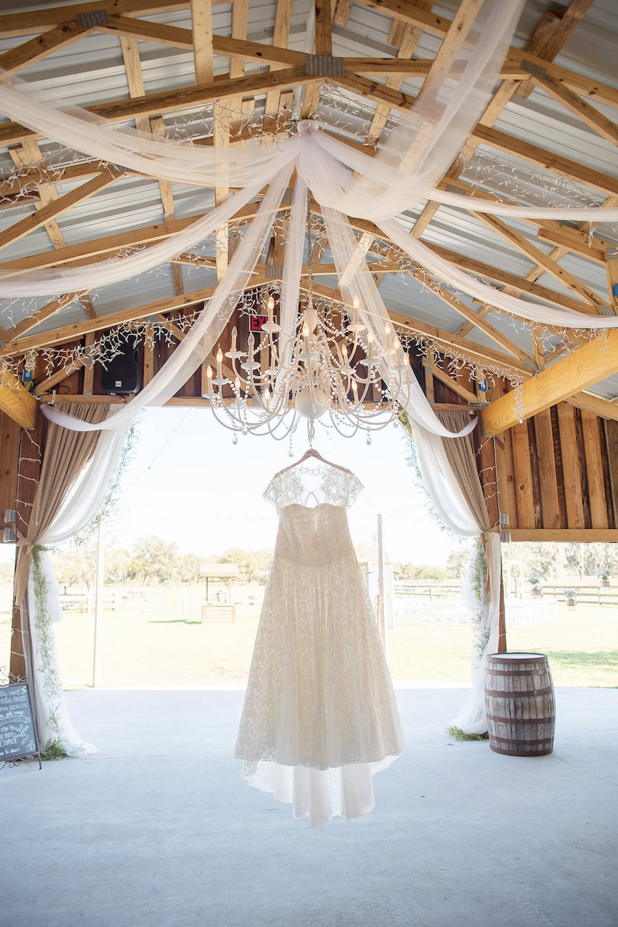 Ivory, Lace Wedding Dress Hung on Chandelier in Wooden Barn