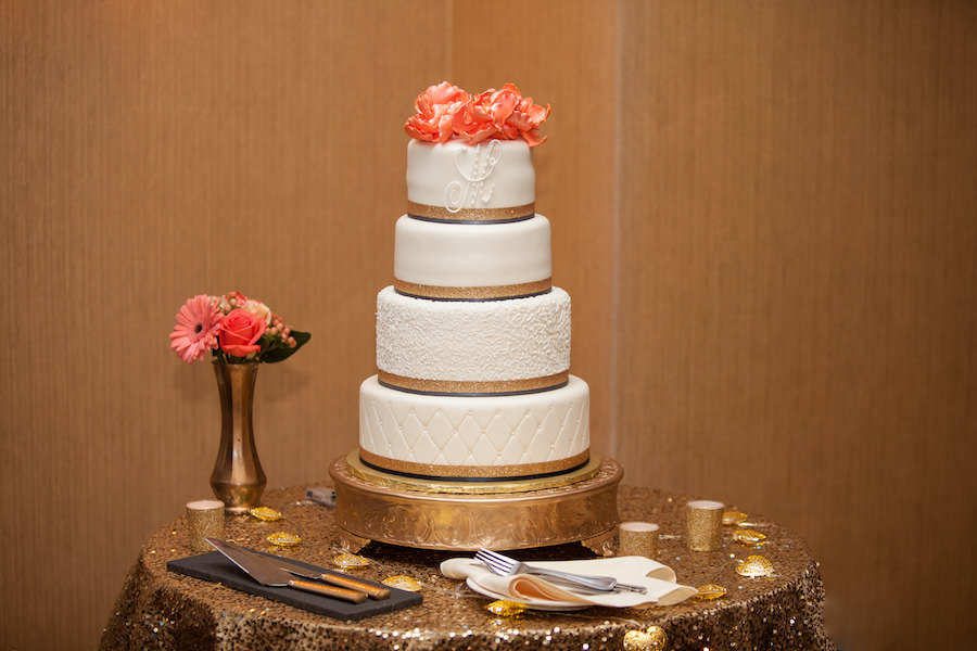 Four Tiered, White Round Wedding Cake with Coral Floral Cake Topper Accent and Monogram on Gold Sequined Linen