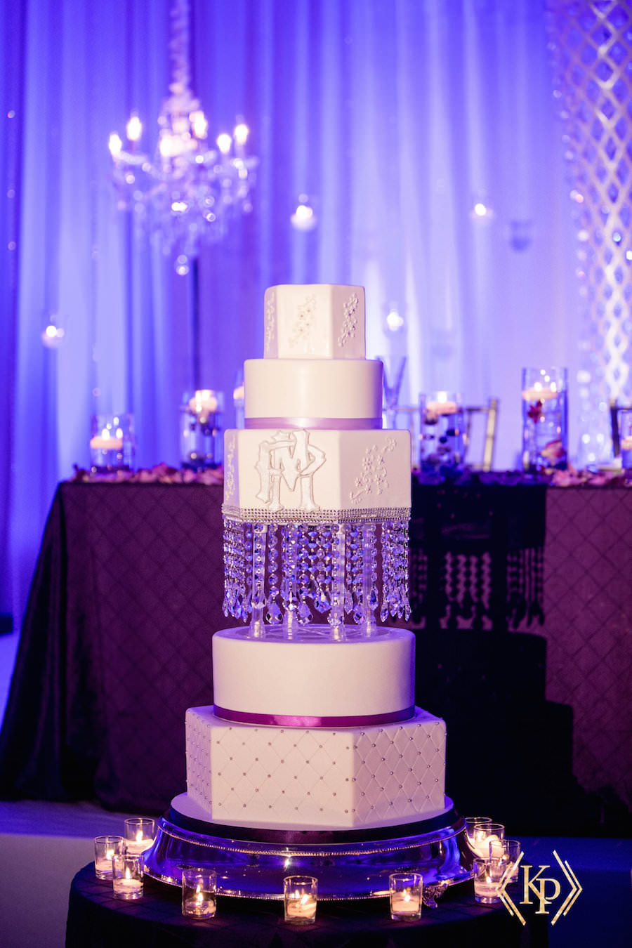 Five Tiered White Geometric Wedding Cake with Monogram and Hanging Decor with Purple Uplight| Tampa Wedding Cakes and Desserts Hands on Sweets