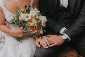 Bride and Groom Wedding Portrait Holding Hands with Peach, Orange, and Ivory Floral Bridal Bouquet with Greenery