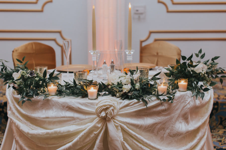 Wedding Reception Sweetheart Table with Green Garland and Ivory Flowers with Candlelight and Blush Linens