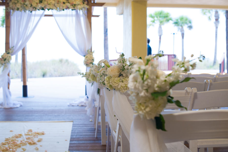 Elegant Beachfront Wedding Ceremony at St. Pete in The Sirata Wedding Venue with White Resin Chairs, Ivory Hydrangea Aisle Bouquets, and Beachwood Wedding Archway with Tulle and Ivory Flowers | St. Petersburg Wedding Photographer Castorina Photography