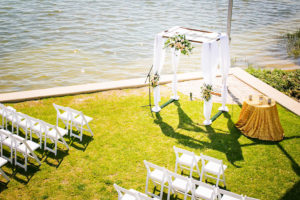 Waterfront St. Petersburg Wedding Ceremony with Draped Arch and Pastel Peach Flowers and White Folding Garden Chairs