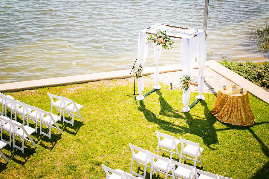 Waterfront St. Petersburg Wedding Ceremony with Draped Arch and Pastel Peach Flowers and White Folding Garden Chairs