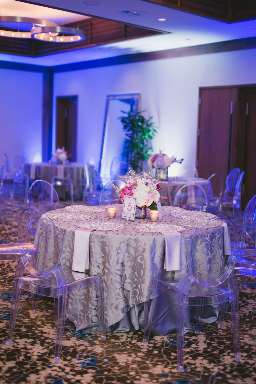 Silver Reception Decor with Pink and White Wedding Centerpieces, Purple Uplighting and Ghost Chairs | Linens by Over the Top Rental Linens | Chargers by Signature Event Rentals | Lighting by Gabro Event Services | Roohi Photography