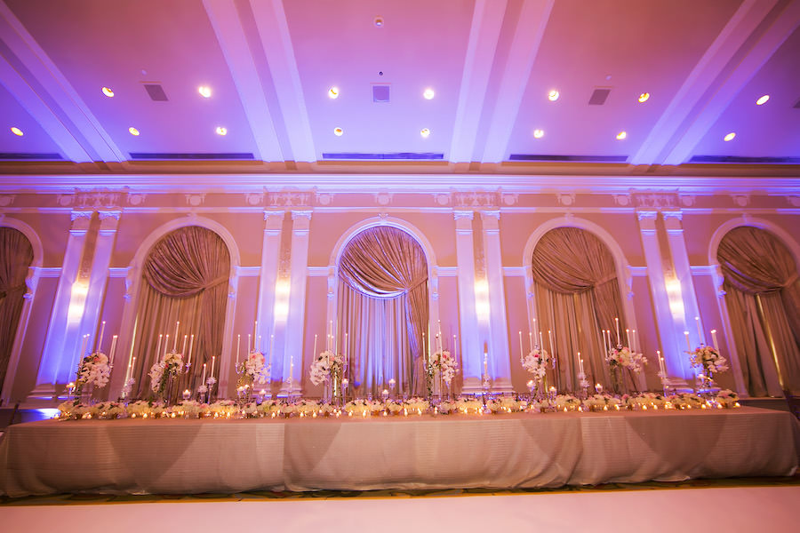 Long Feasting Wedding Head Table with Gold Linens and Tall Ivory Centerpieces and Tall Taper White Candles and Pink Uplighting at Downtown St Petersburg Wedding Venue Vinoy Renaissance Sunset Ballroom | St. Pete Wedding Photographer Limelight Photography