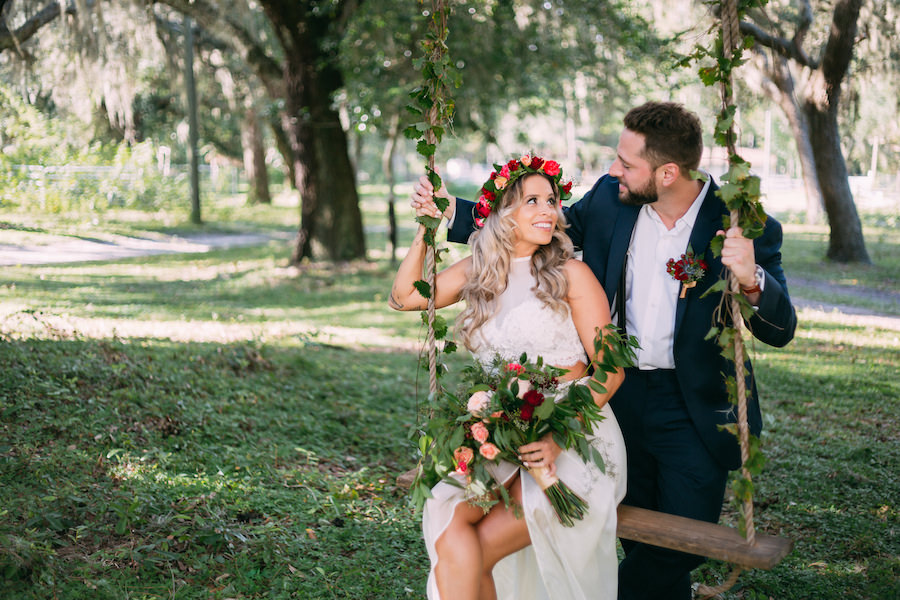 Bohemian Chic Inspired Wedding Portrait with Bride with Floral Crown Headpiece and Groom with Navy Suit on Swing at The Barn at Crescent Lake