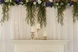 Rustic Glam Ivory Candles On Ivory Mantle with Cascading Greenery and Pipe and Drape with Twinkle Lights at Tampa Bay Wedding Venue Cross Creek Ranch