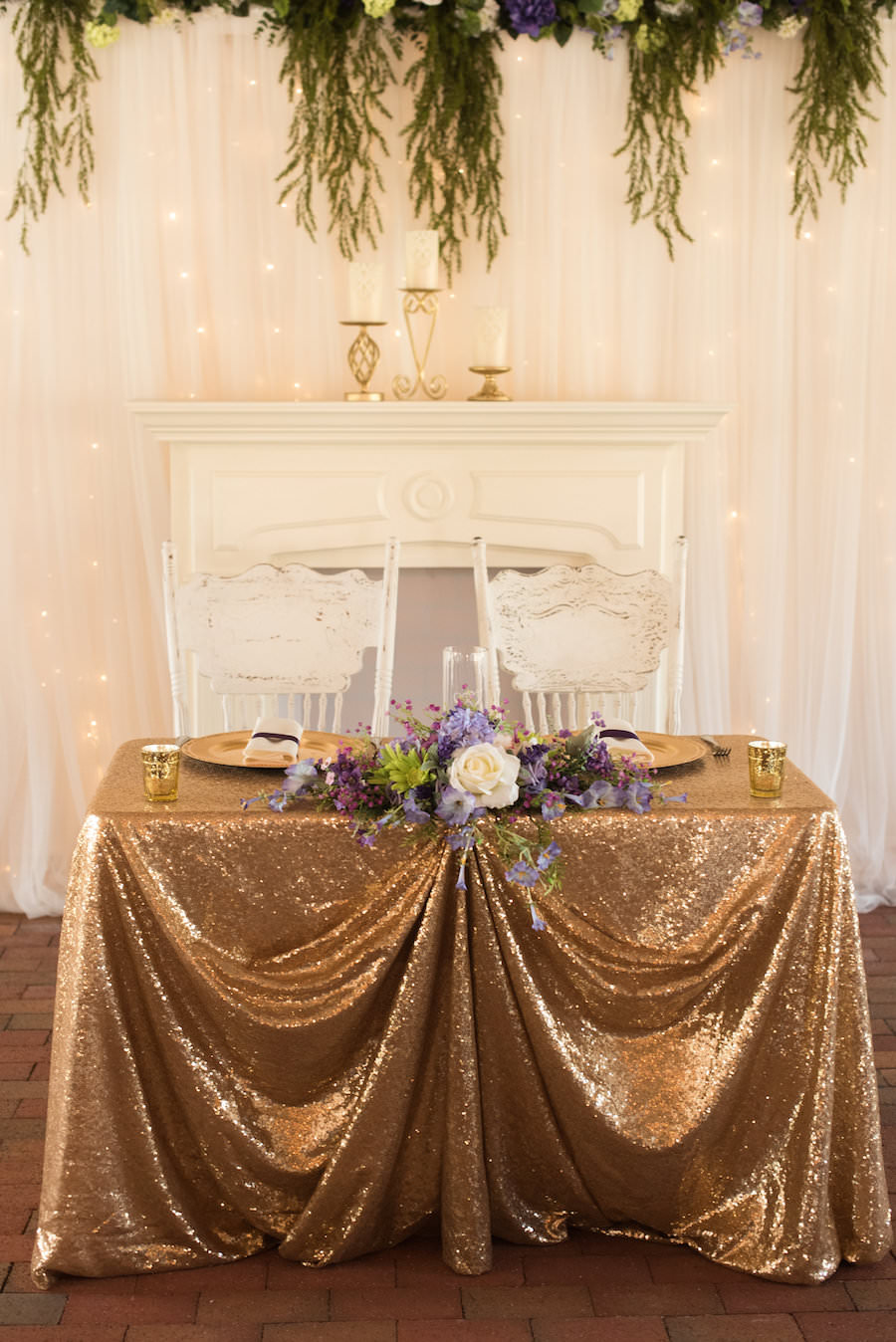 Bride and Groom Rustic Glam Sweetheart Table with Gold Sequin Linen and Purple and Ivory Centerpieces and Vintage Chairs at Tampa Wedding Venue Cross Creek Ranch