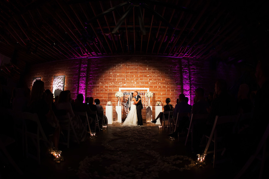 Bride and Groom First Kiss at Indoor, Wedding Ceremony with Exposed Brick Walls and Purple Uplighting | Modern Wedding Ceremony Ideas | St. Petersburg Wedding Venue NOVA 535 | Wedding Photographer Limelight Photography