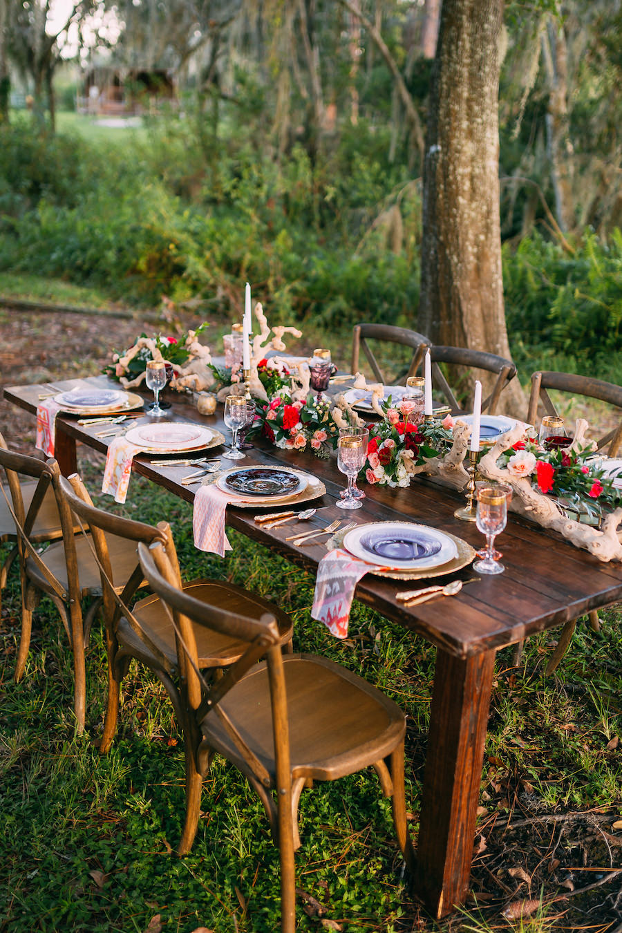 Long Farm Table Feasting Table with Boho Chic Inspired Garland with Wooden Centerpiece and Vintage Glasses, Chargers and Cross Back Farm Chairs | Ever After Vintage Weddings Tampa Bay Wedding Rental Company with Chairs from A Chair Affair