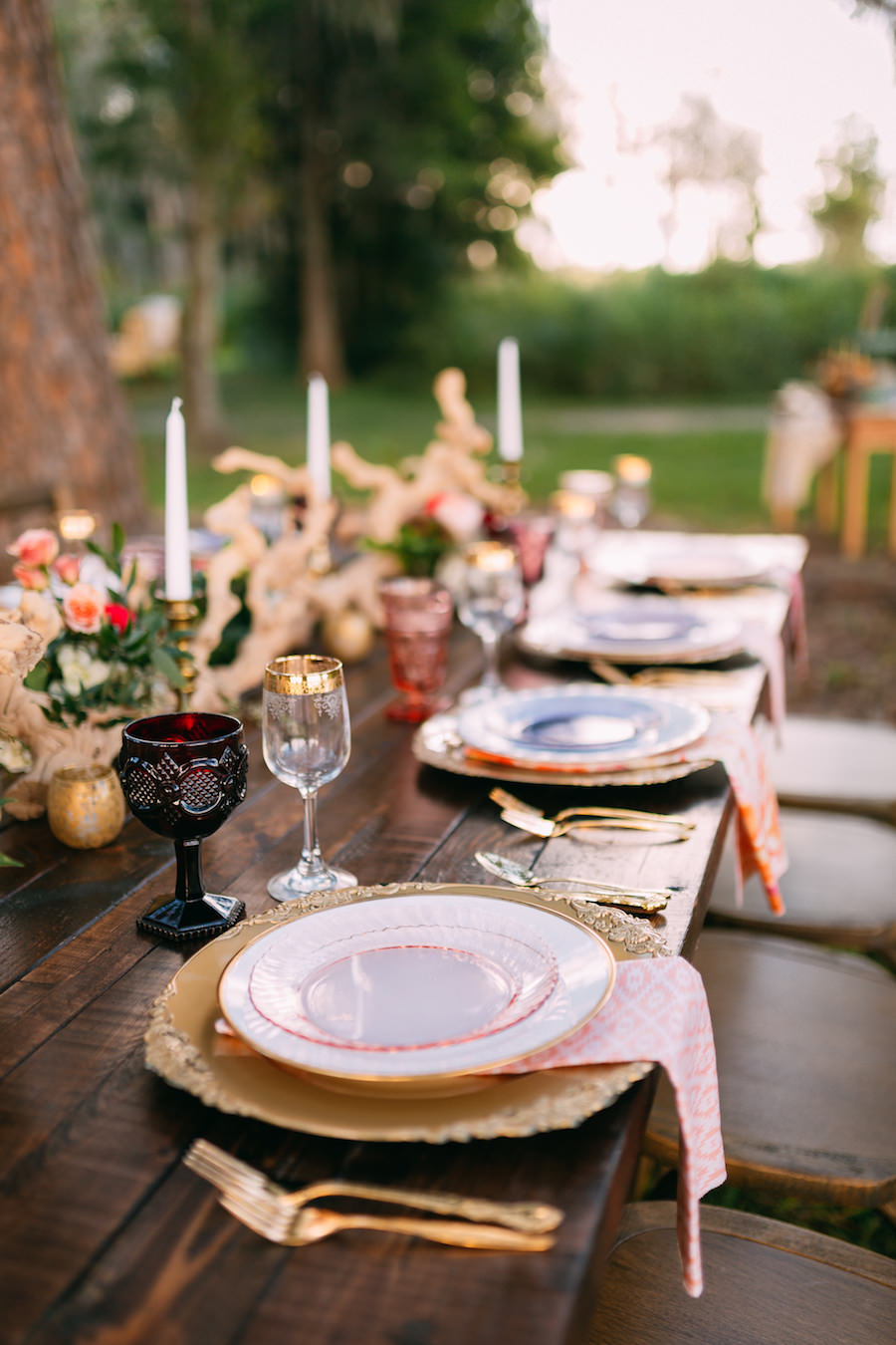 Boho Chic Wedding Reception Placesetting | Long Farm Table Feasting Table with Boho Chic Inspired Garland with Wooden Centerpiece and Vintage Glasses, Chargers and Cross Back Farm Chairs | Ever After Vintage Weddings Tampa Bay Wedding Rental Company