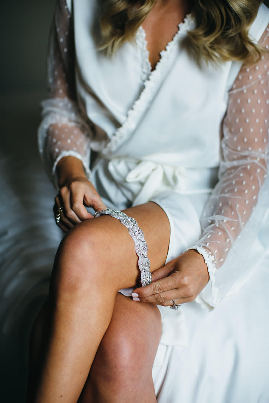 Bridal Getting Ready Wedding Portrait in White Lace Robe Putting On Rhinestone Garter Belt