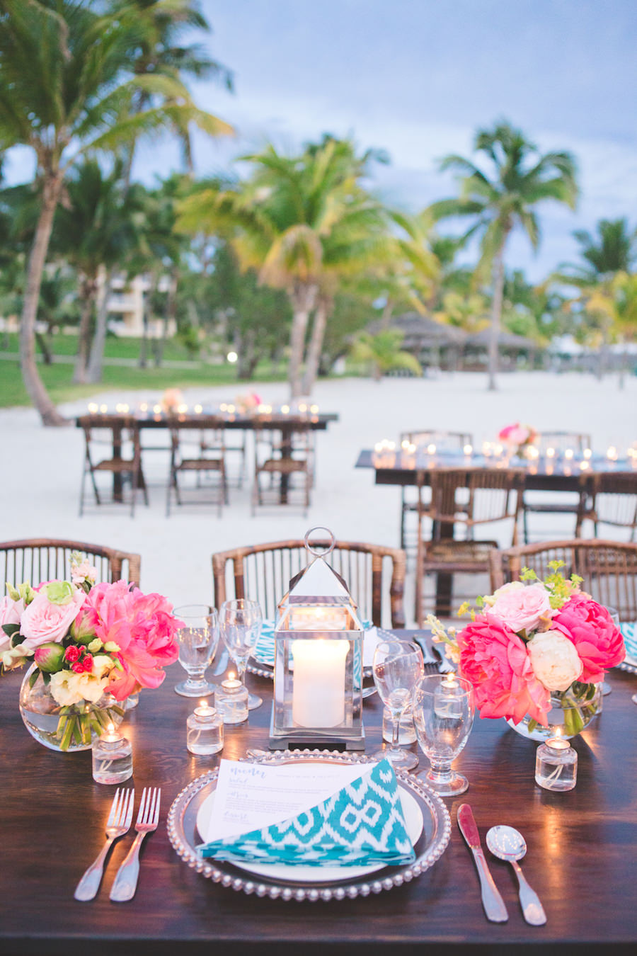 Bahamas Destination Beach Caribbean Reception Venue with Farm Tables, Bamboo Seating, Turquoise Green Napkins, Bright Pink Centerpieces and Candlelight | Aisle Society Weddings Abaco Beach Resort