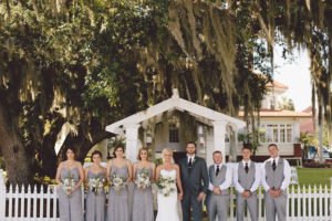 Outdoor Bridal Party Wedding Portrait | Grey Beaded Adrianna Papell Bridesmaid Dresses and White Sweetheart Robert Bullock Lace Trumpet Wedding Dress with Ivory and Grey Wedding Bouquets | Grey and Gold Wedding Ideas| Vintage Outdoor Wedding Ceremony under Spanish Moss Tree with White Resin Folding Chairs and White French Door Arched Doorway Altar | Sarasota Rentals by Reserve Vintage Rentals | Waterfront Sarasota Wedding Venue Palmetto Riverside Bed and Breakfast