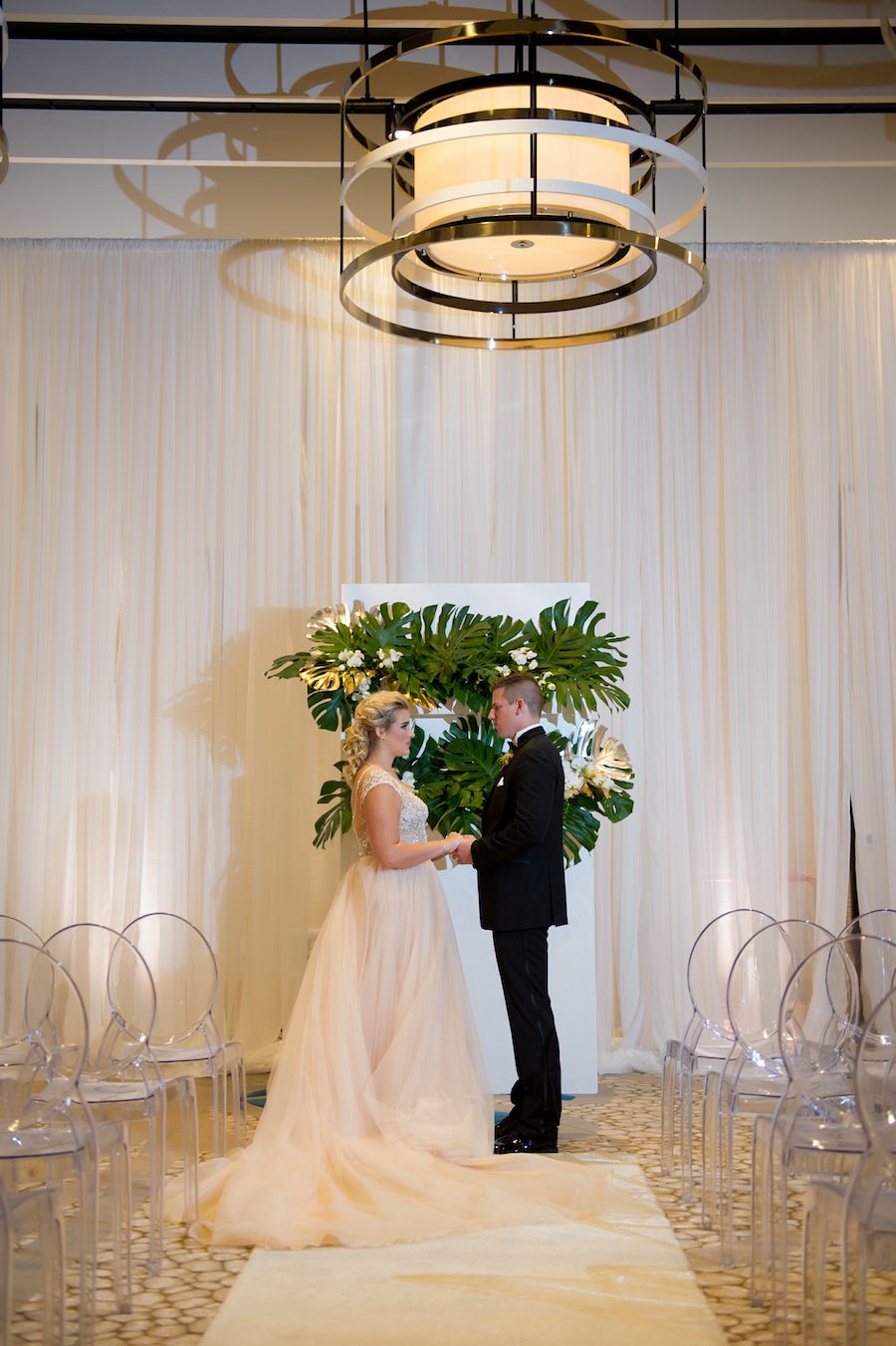 Ballroom Wedding Ceremony with Draping by Gabro Event Services, Ghost Chairs from A Chair Affair and Palm Leaf Ceremony Altar Backdrop | Hotel Wedding Venue Wyndham Grand Clearwater Beach | Andi Diamond Photography | Wedding Planner Parties a la Carte