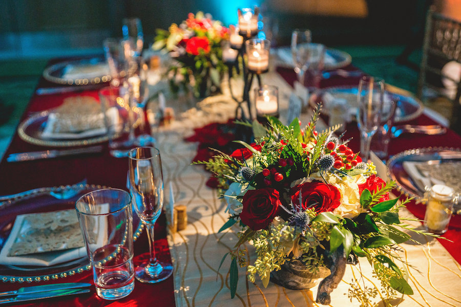 Ballroom Tampa Bay Indoor Wedding Reception with Long Feasting Tables, Red Rose Floral Centerpiece Decor and Beaded Glass Chargers | Waterfront Wedding Venue Hyatt Regency Clearwater Beach | Wedding Planner Special Moments Event Planning | Apple Blossom Floral Designs | Signature Event Rentals