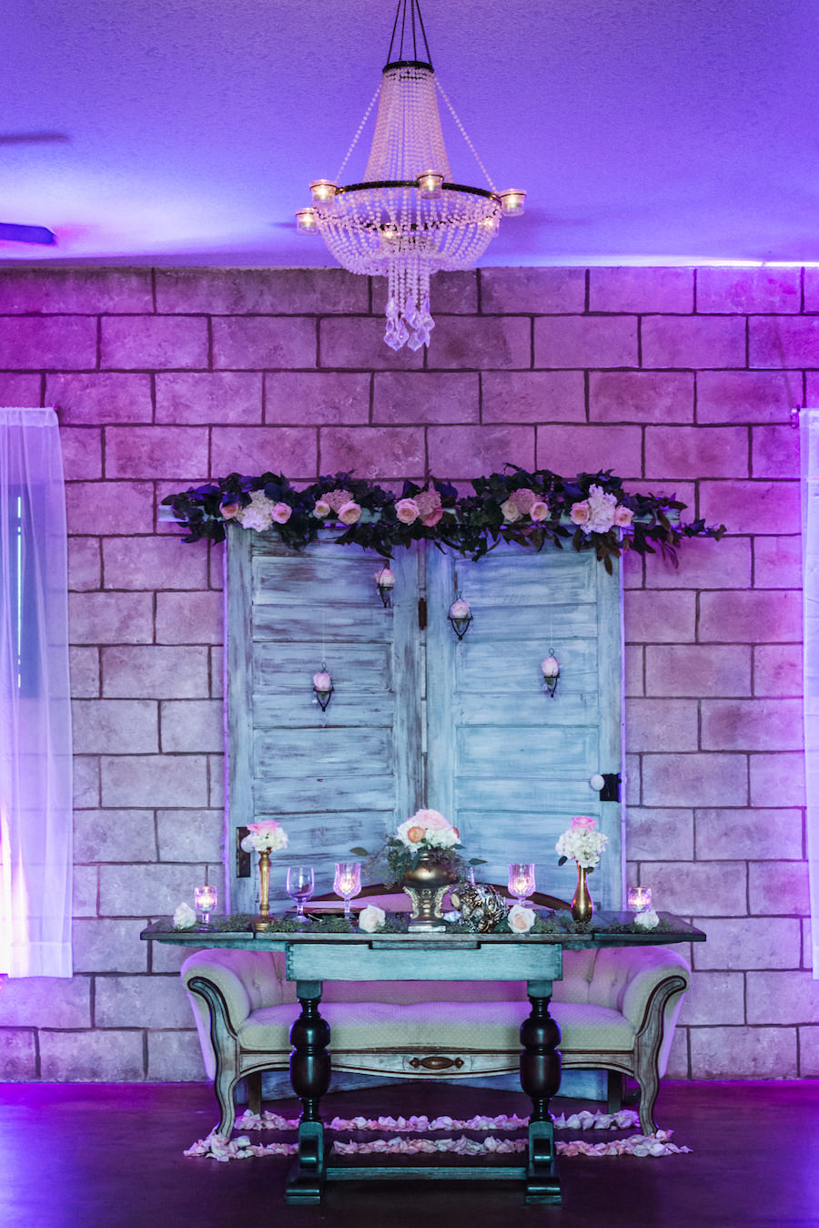 Wedding Reception Sweetheart Table Decor with Distressed, Wooden Doors, Vintage Cream Settee, White and Pink Floral Centerpieces and Purple Uplighting | Elegant Rustic Wedding Inspiration