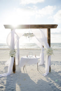 Wedding Ceremony Wooden Arch with White Drapery and Crystal Chandelier with Ivory Flowers | Clearwater Beach Wedding Planner Kimberly Hensley Events